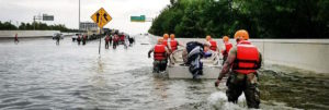 Hurricane Harvey flood rescue team with boat wading through knee-high water on flooded highway